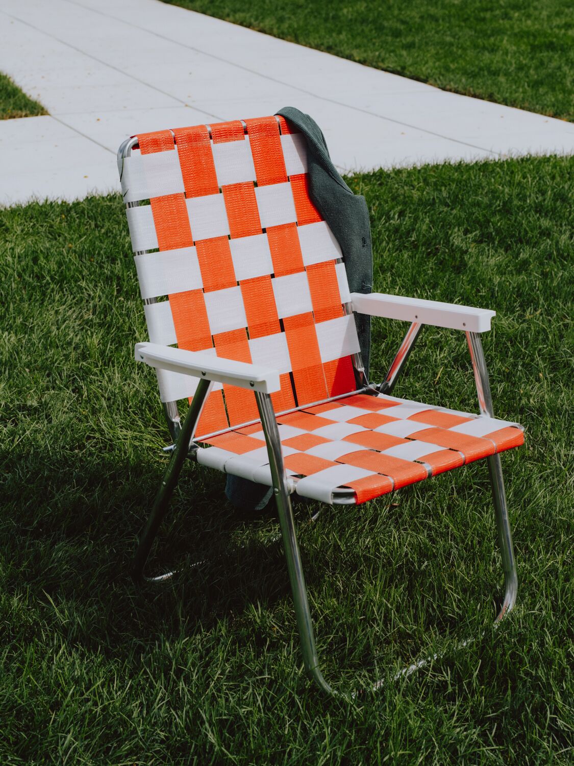 A chair with a checkered orange and white fabric, metal frame, and a dark green strap.