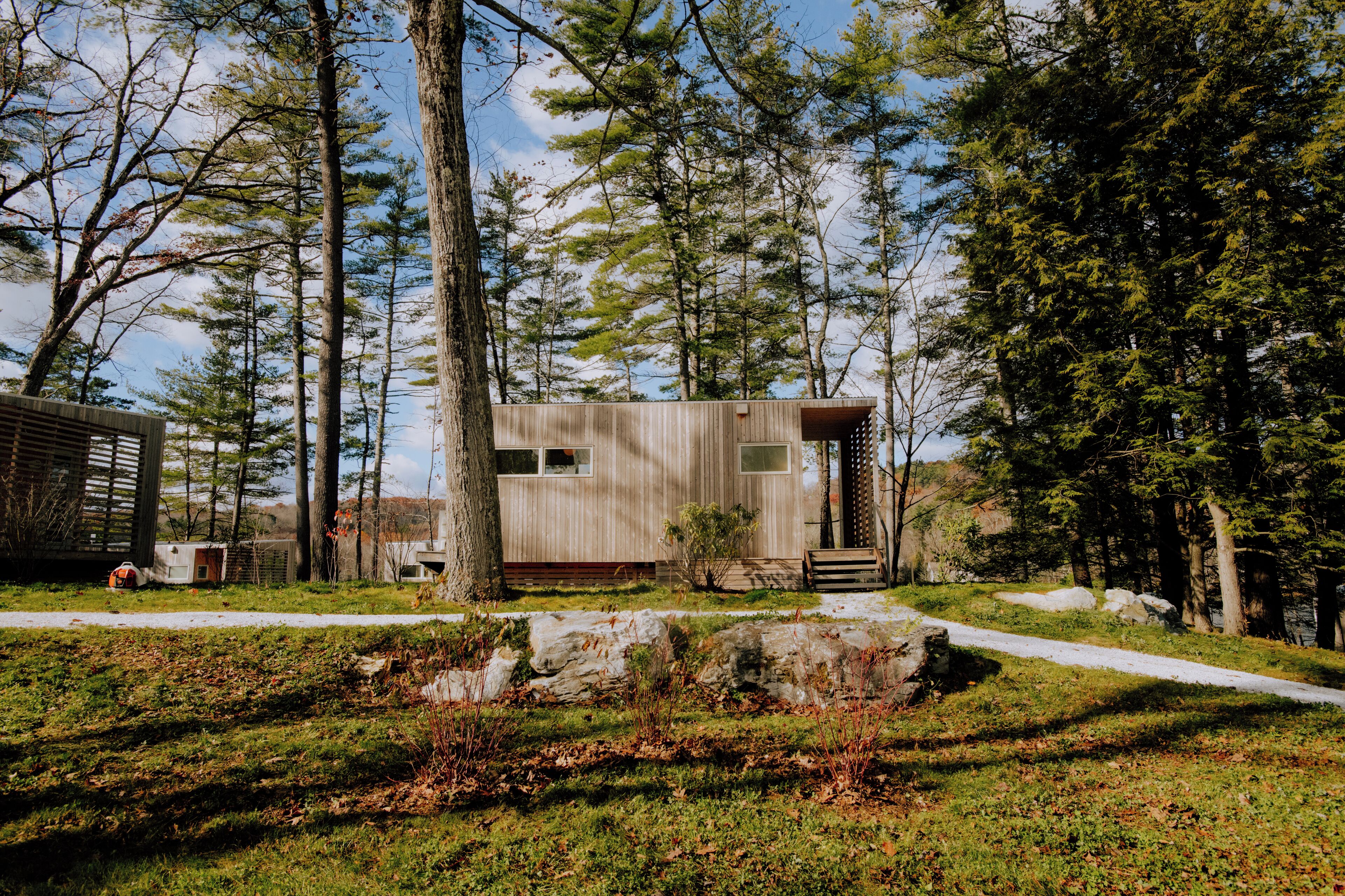 A modern cabin with a wooden exterior, surrounded by trees and a grassy area.