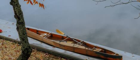 A canoe on a dock by a calm lake with autumn leaves on the ground.