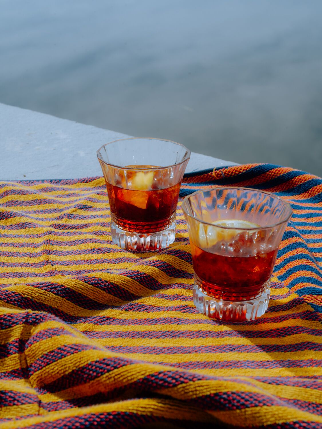 Två glas med en bärnstensfärgad dryck står på ett färgglatt, randigt tyg.