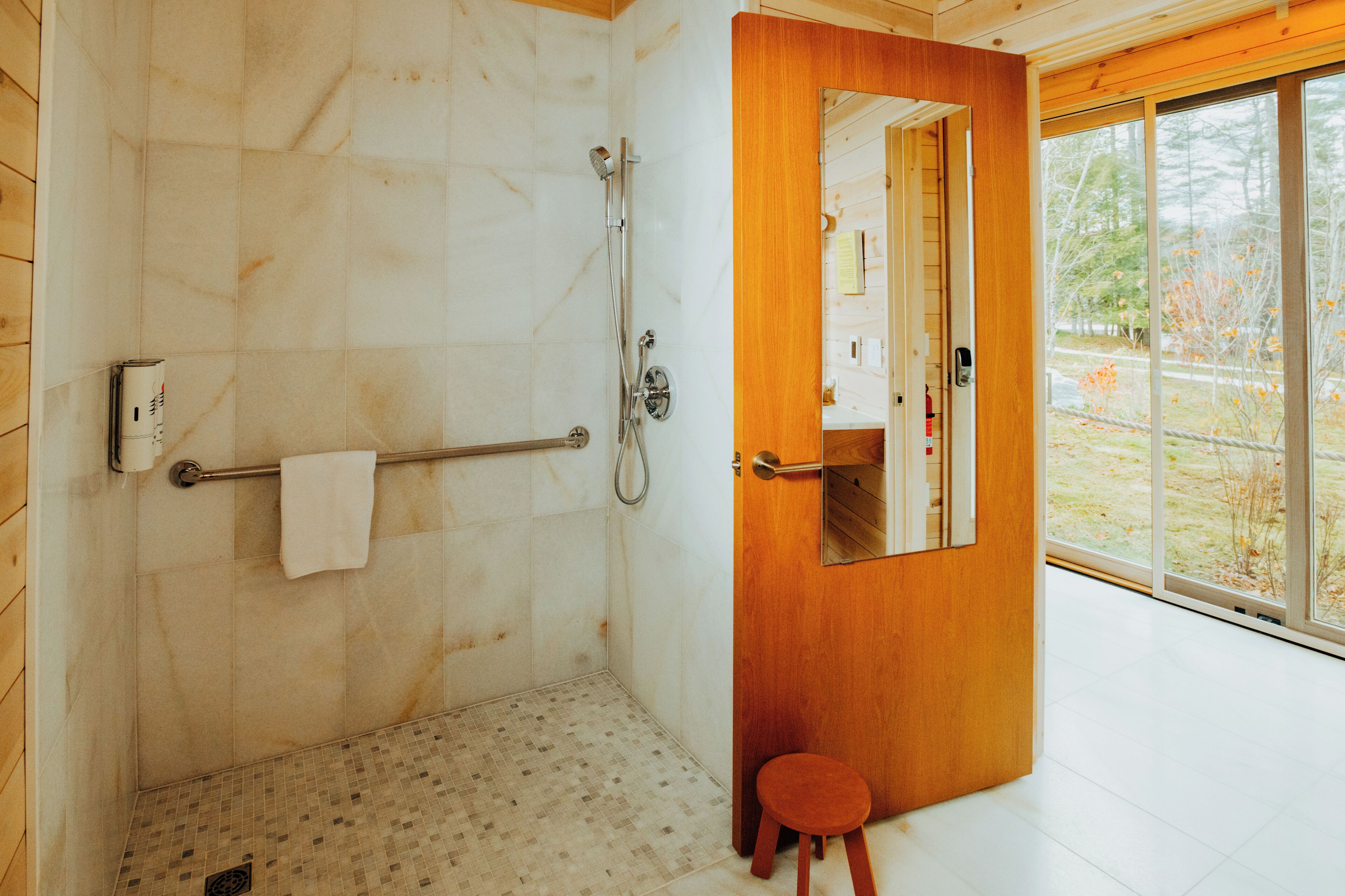 A modern bathroom with a shower, a towel rack, and a small stool.