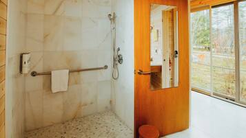 A modern bathroom with a shower, a towel rack, and a small stool.