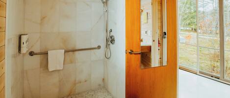 A modern bathroom with a shower, a towel rack, and a small stool.