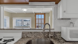 A kitchen with a granite countertop, stainless steel sink, white gas stove, and a white microwave.