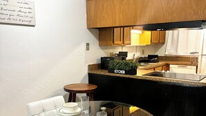 A dining area with a glass table and white chairs, a kitchen in the background, and a handwritten note on the wall. - Cozy 2-bedroom condo with WiFi, AC in quiet NW Gainesville, FL (Gainesville)