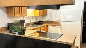 A modern kitchen with wooden cabinets, a black countertop, a built-in stove, a sink, and a refrigerator. - Cozy 2-bedroom condo with WiFi, AC in quiet NW Gainesville, FL (Gainesville)