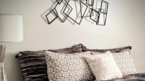 Una cama bien hecha con ropa de cama estampada, una mesita de noche con lámpara y una obra de arte en la pared.