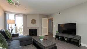 A modern living room with a sectional sofa, a flat-screen TV, a fireplace, and a large window.
