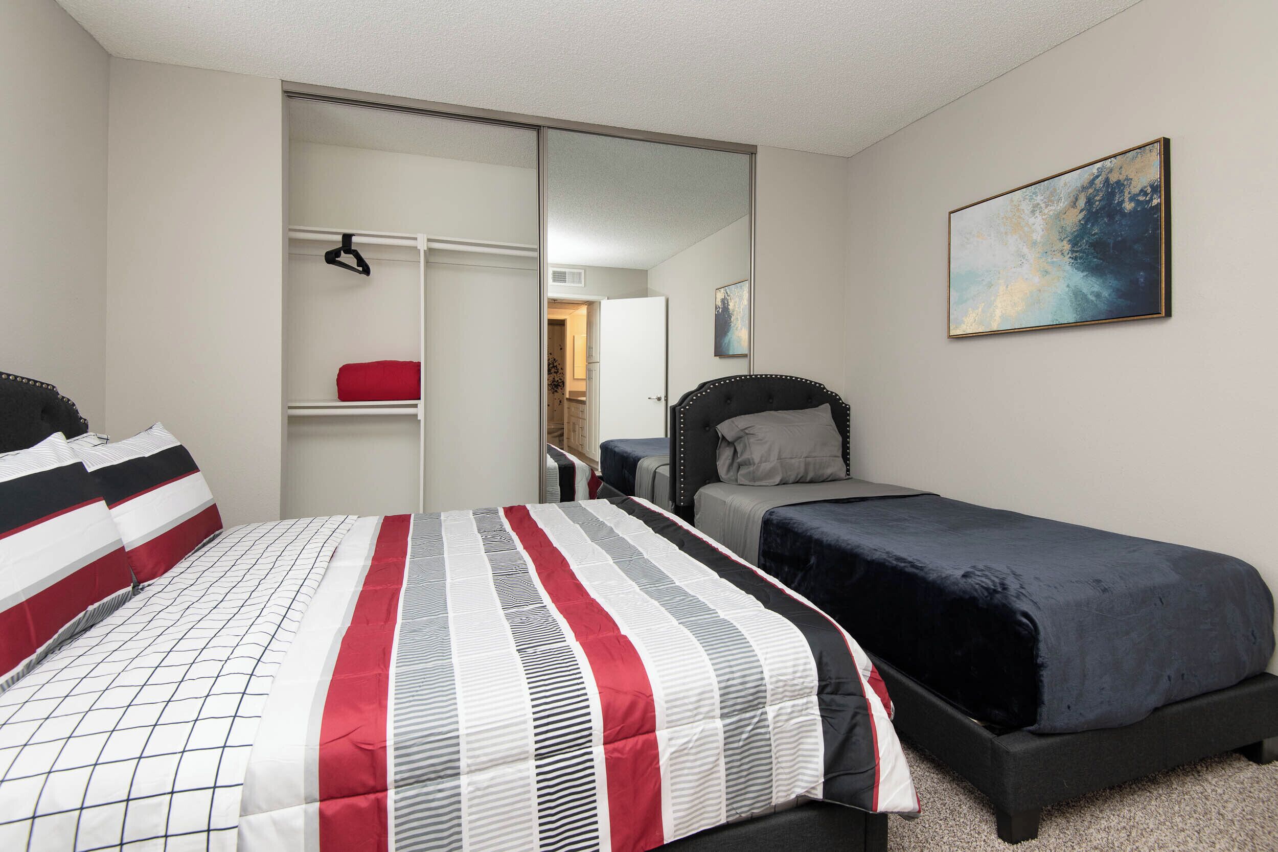 A bedroom with a bed, a smaller bed, a wardrobe, and a painting on the wall.