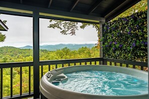 A hot tub on a balcony with a view of a forested mountain range.