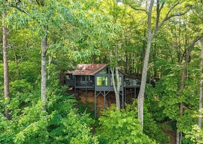 A cabin with a deck, surrounded by dense forest.