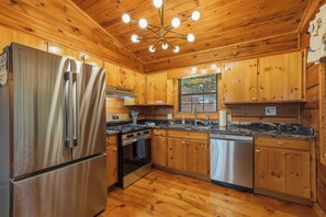 A compact kitchen with wooden cabinets, a stainless steel refrigerator, a stove, and a dishwasher.