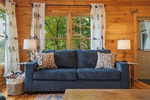 A cozy room with a blue sofa, patterned pillows, two lamps, and a window with curtains.