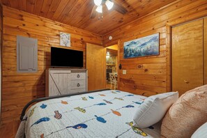 A wooden cabin room with a bed, a television, a painting, and a stone fireplace.