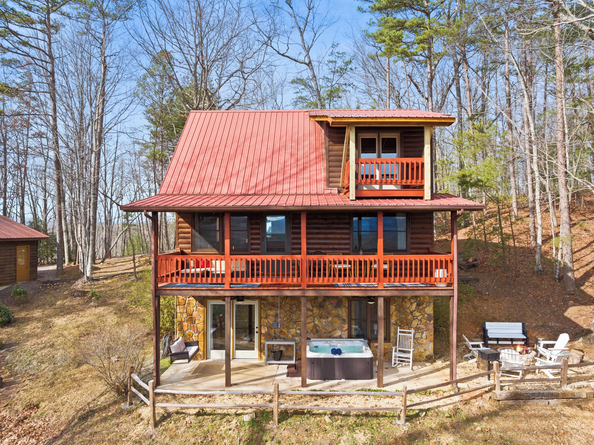 Une cabane en rondins à deux étages, avec un toit rouge, un balcon et un jacuzzi au rez-de-chaussée.