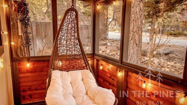 A hanging chair with a cushioned seat in a wooden room with large windows.