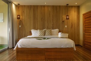 Un dormitorio con cabecera de madera, cama con sábanas blancas, dos lámparas de pared y una puerta de madera.