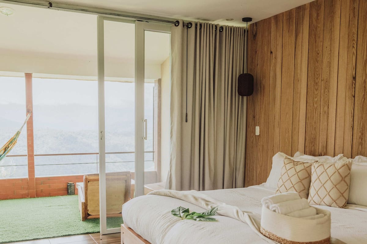 Une chambre avec un grand lit, des murs en bois, une vue sur l’extérieur et un tapis vert sur le sol.
