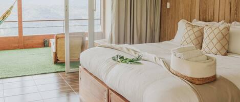 A bedroom with a large bed, wooden walls, a view of the outdoors, and a green mat on the floor.