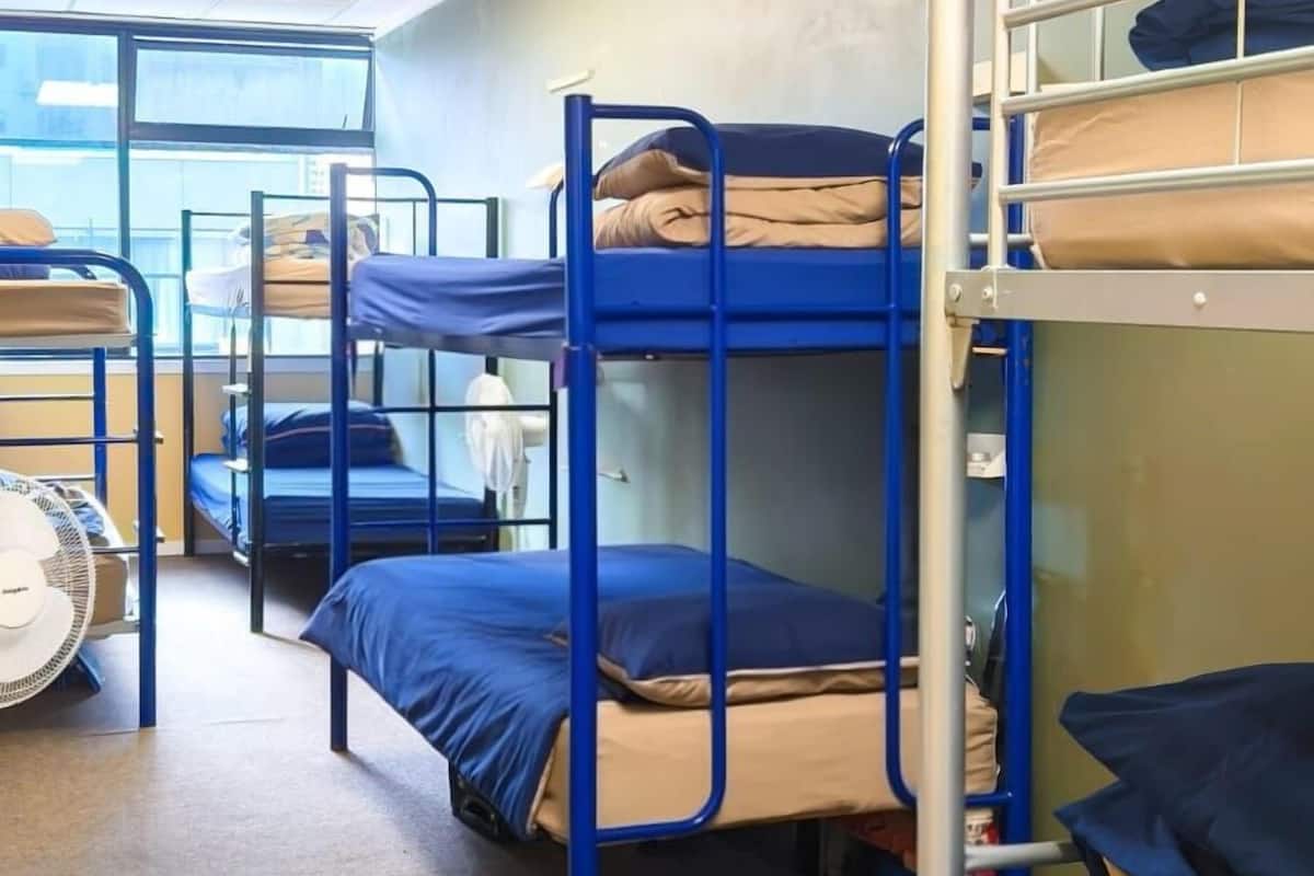 A dormitory room with bunk beds, a fan, and a window.