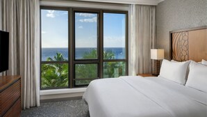 Une chambre d’hôtel dotée d’une grande fenêtre donnant sur l’océan et les palmiers.