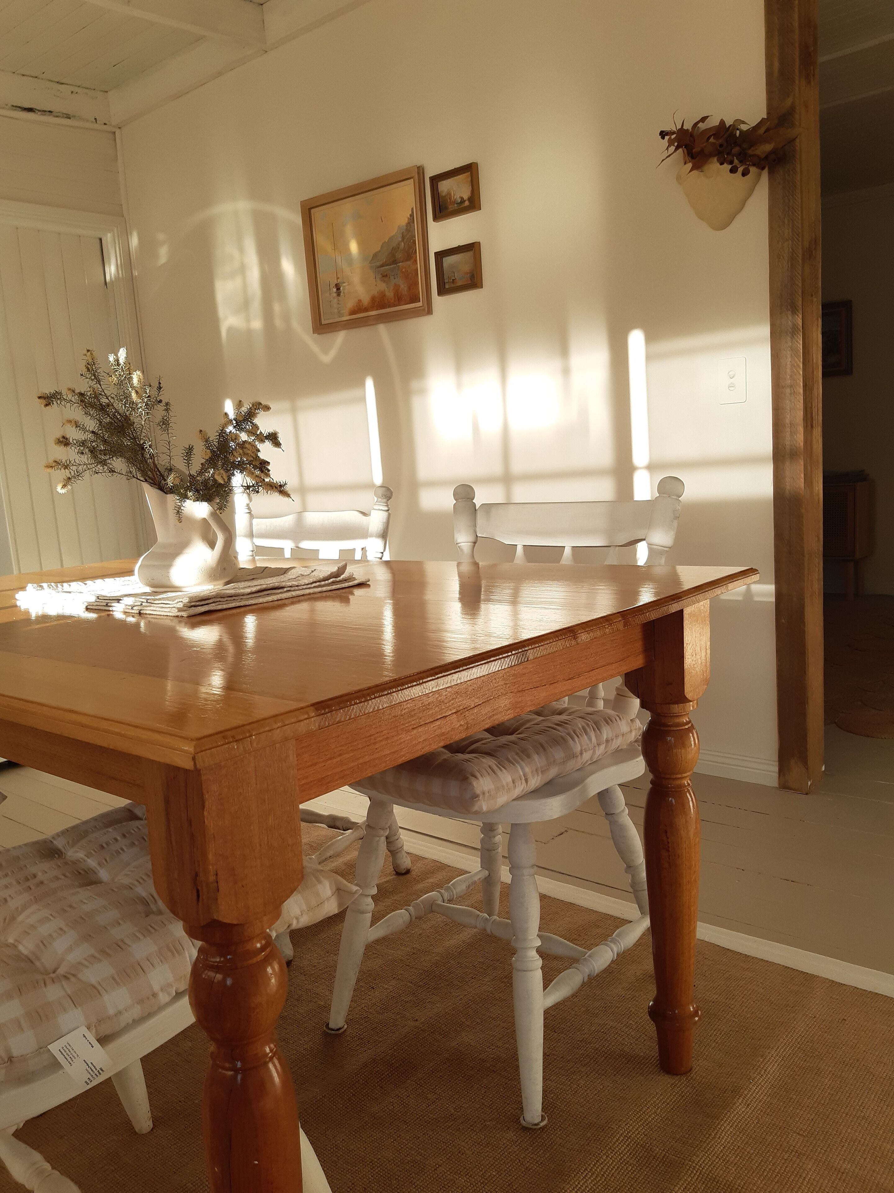 A wooden dining table with a bench, white chairs, and a vase with flowers on a rug.