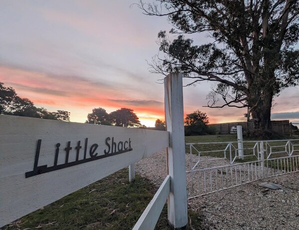 Un letrero de madera con la inscripción 'Little Shack', un árbol y una cerca.
