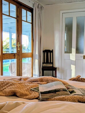 Una habitación con cama, una silla, una puerta con cristal esmerilado y vista a zonas verdes.