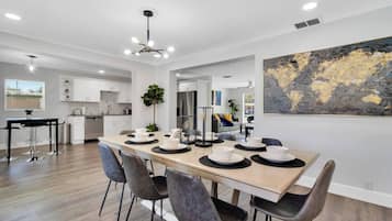 Une cuisine moderne avec des meubles blancs, un coin repas doté d’une longue table et de chaises, et un grand tableau abstrait accroché au mur.