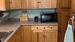 A compact kitchen with wooden cabinets, a built-in microwave, and a stainless steel sink. - Private, secluded 2-bedroom house with King, Queen beds near Cable with WiFi, AC (Cable)