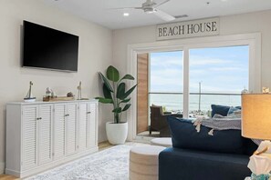 Una habitación con televisor grande, un armario, una planta, un sofá y vista al océano.