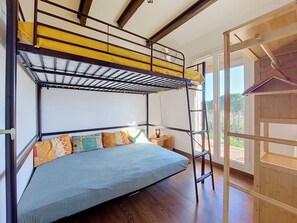 Ein Etagenbett mit einer Leiter, ein Nachttisch mit einer Lampe und Blick ins Freie.