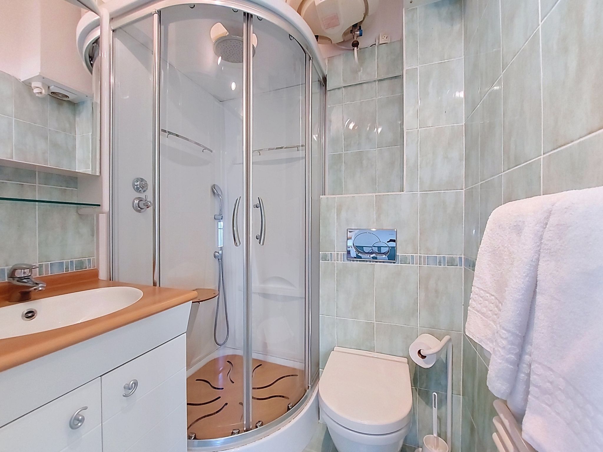 Un baño moderno con ducha envuelta en vidrio, tocador de madera, inodoro y perchero para toallas.