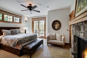 A bedroom with a large bed, a bench, a fireplace, and a ceiling fan.