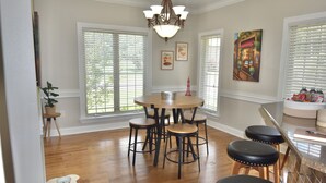 A dining area with a round table surrounded by four stools, a chandelier, and two windows with blinds. - Spacious 4 Bed Island House on Lake Hamilton with Boat Slip (Hot Springs)