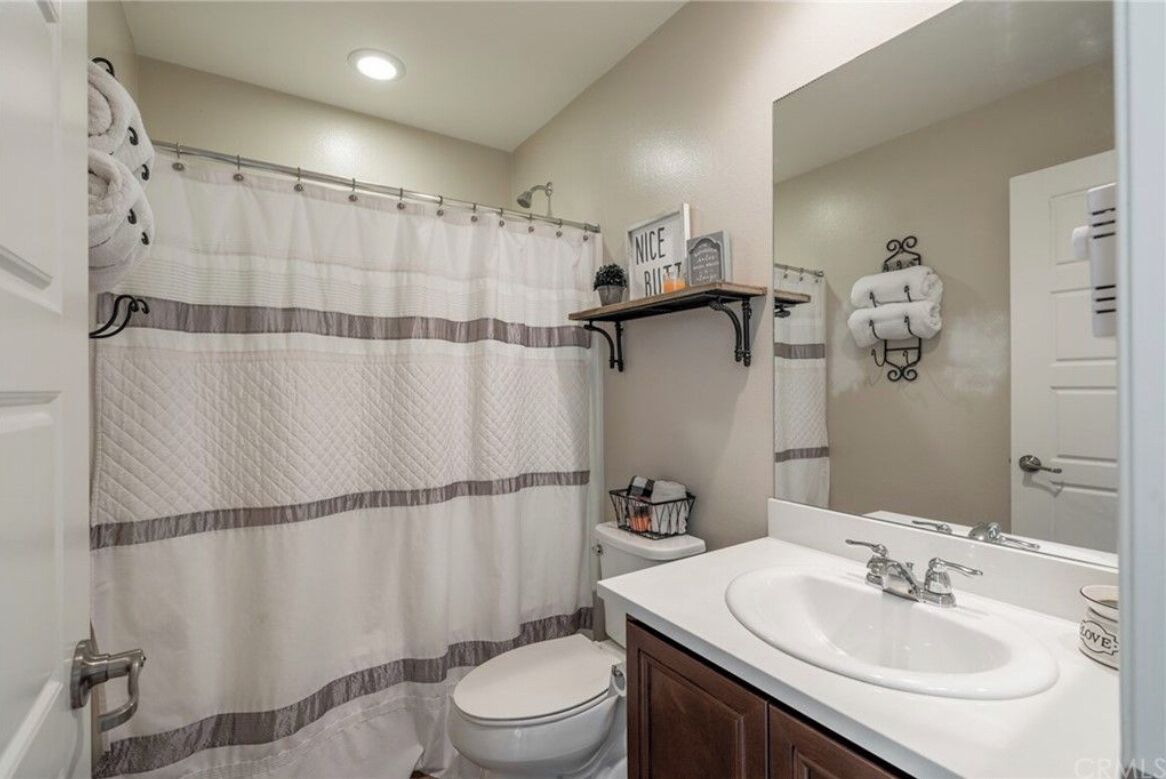 A bathroom with a striped shower curtain, a toilet, a sink with a mirror, and towel racks.
