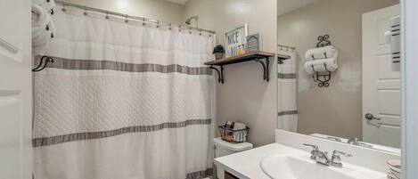 A bathroom with a striped shower curtain, a toilet, a sink with a mirror, and towel racks.
