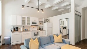 Une cuisine moderne avec des meubles blancs, un canapé bleu agrémenté de coussins jaunes et un grand miroir.