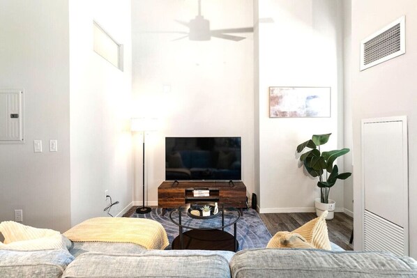 A living room with a flat-screen TV, a ceiling fan, a potted plant, and a sofa.