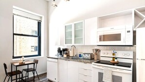 Une cuisine moderne avec des armoires blanches, un four à micro-ondes encastré, une cuisinière et un coin repas comprenant une table et des chaises.