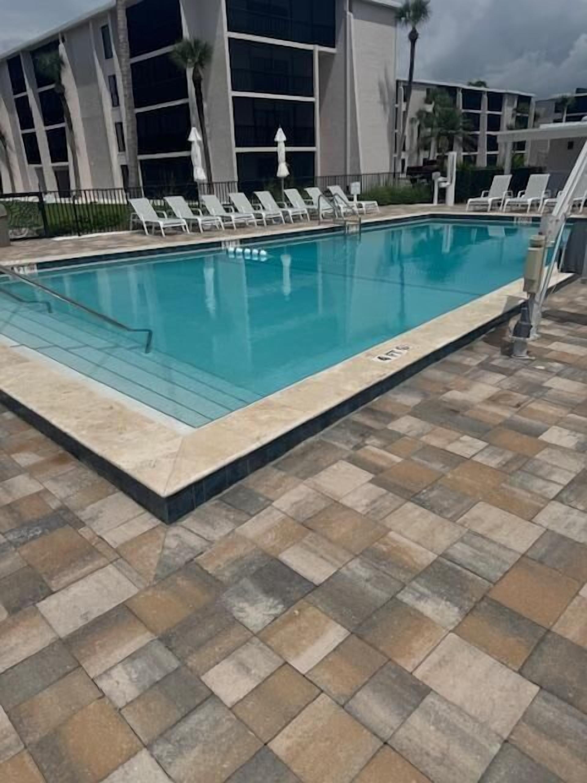 A swimming pool with lounge chairs and a tiled deck.