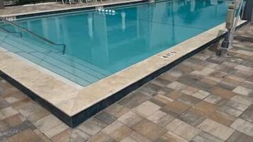 A swimming pool with lounge chairs and a tiled deck.
