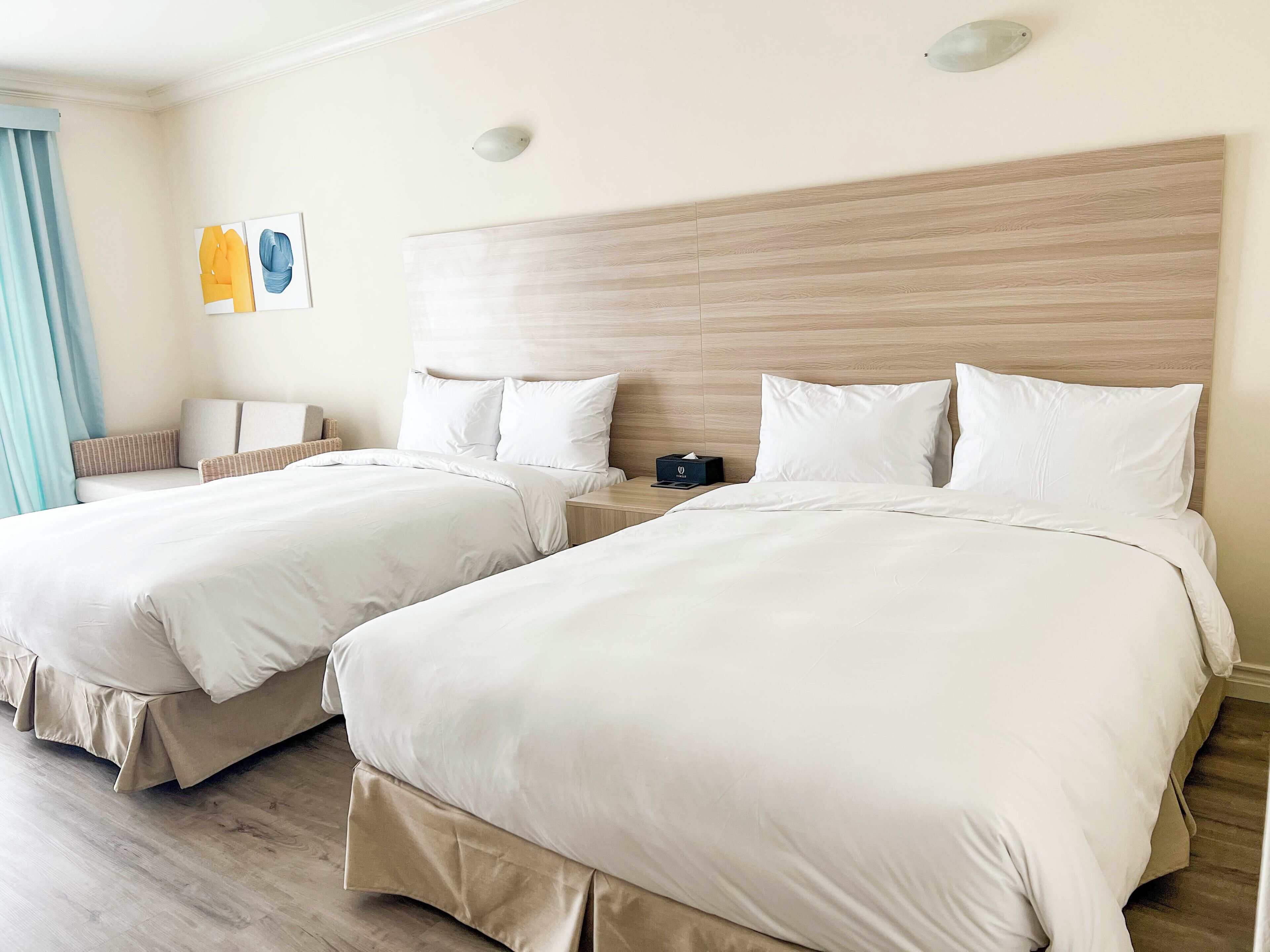 Habitación de hotel con dos camas, una mesita de noche, una lámpara y una ventana con cortinas.