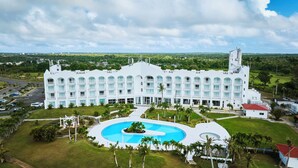 Un hotel grande y blanco con varios balcones, una piscina central y vistas del paisaje circundante.