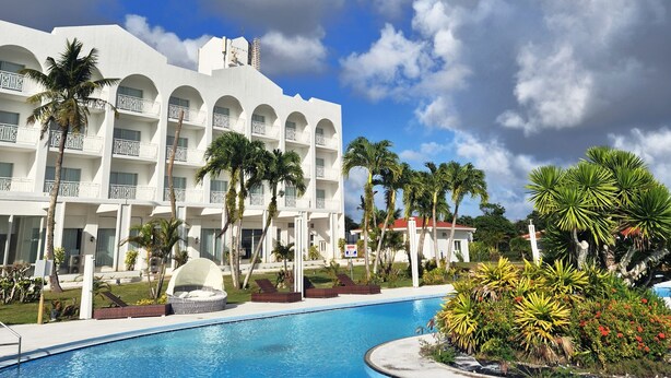 Un resort con piscina, palmeras y un edificio grande de color blanco con balcones.