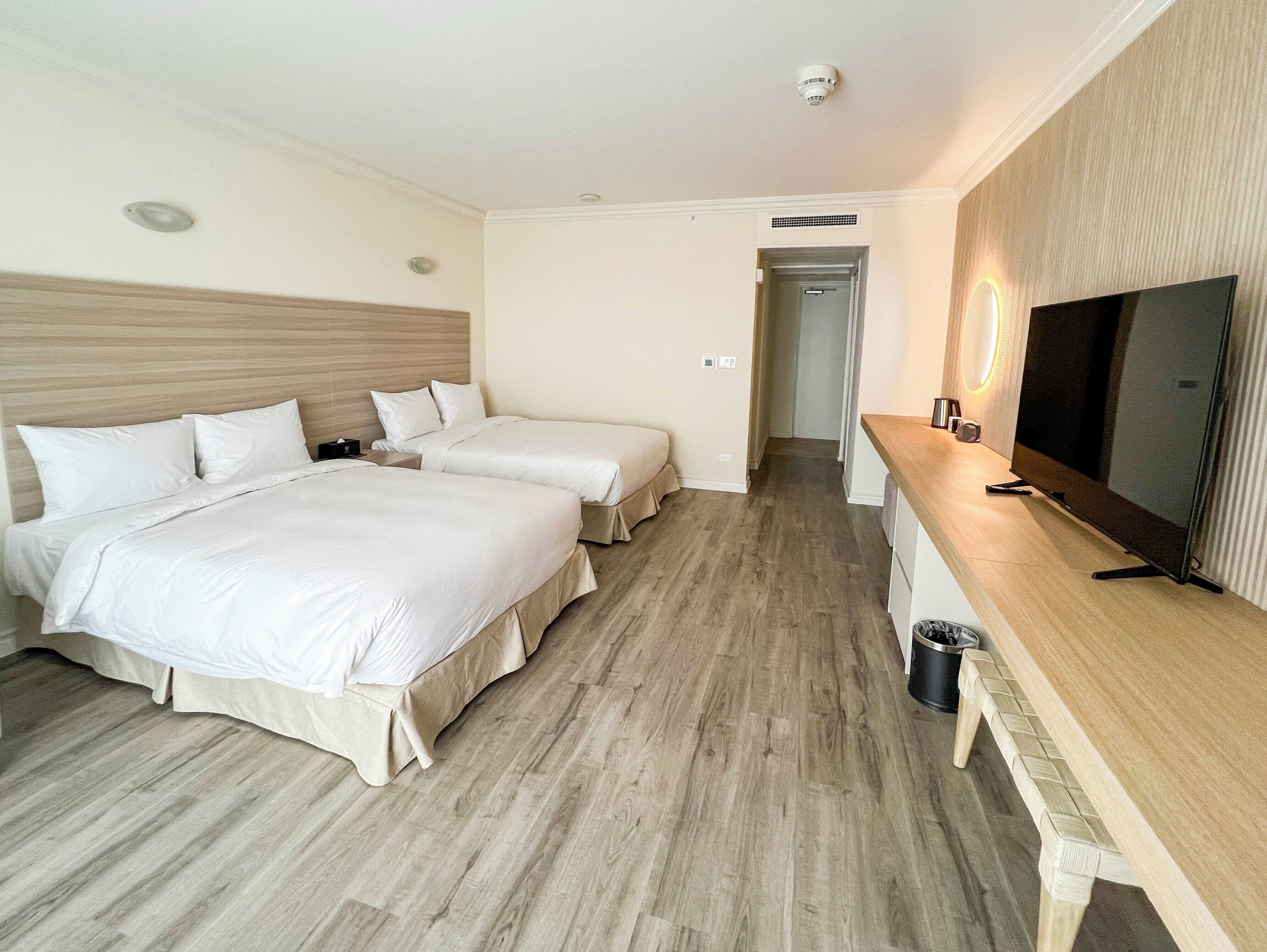 Habitación de hotel con dos camas, televisión, escritorio y espejo.