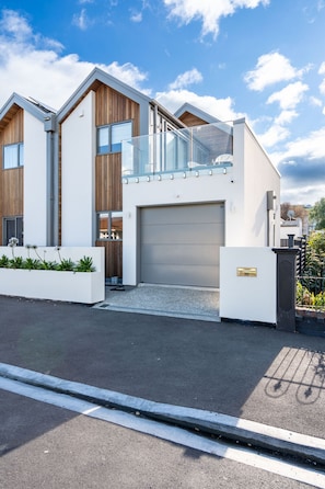 A modern two-story house with a garage, a balcony with glass railings, and a white exterior. - Seaside Luxe in St CLair (Dunedin)