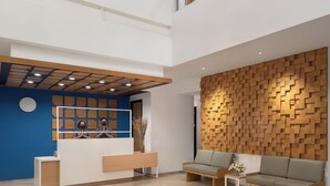 A modern reception area with a blue wall, wooden reception desk, and a seating area with two sofas and a small table. - Hotel 88 Blok M Jakarta by WH (Jakarta)