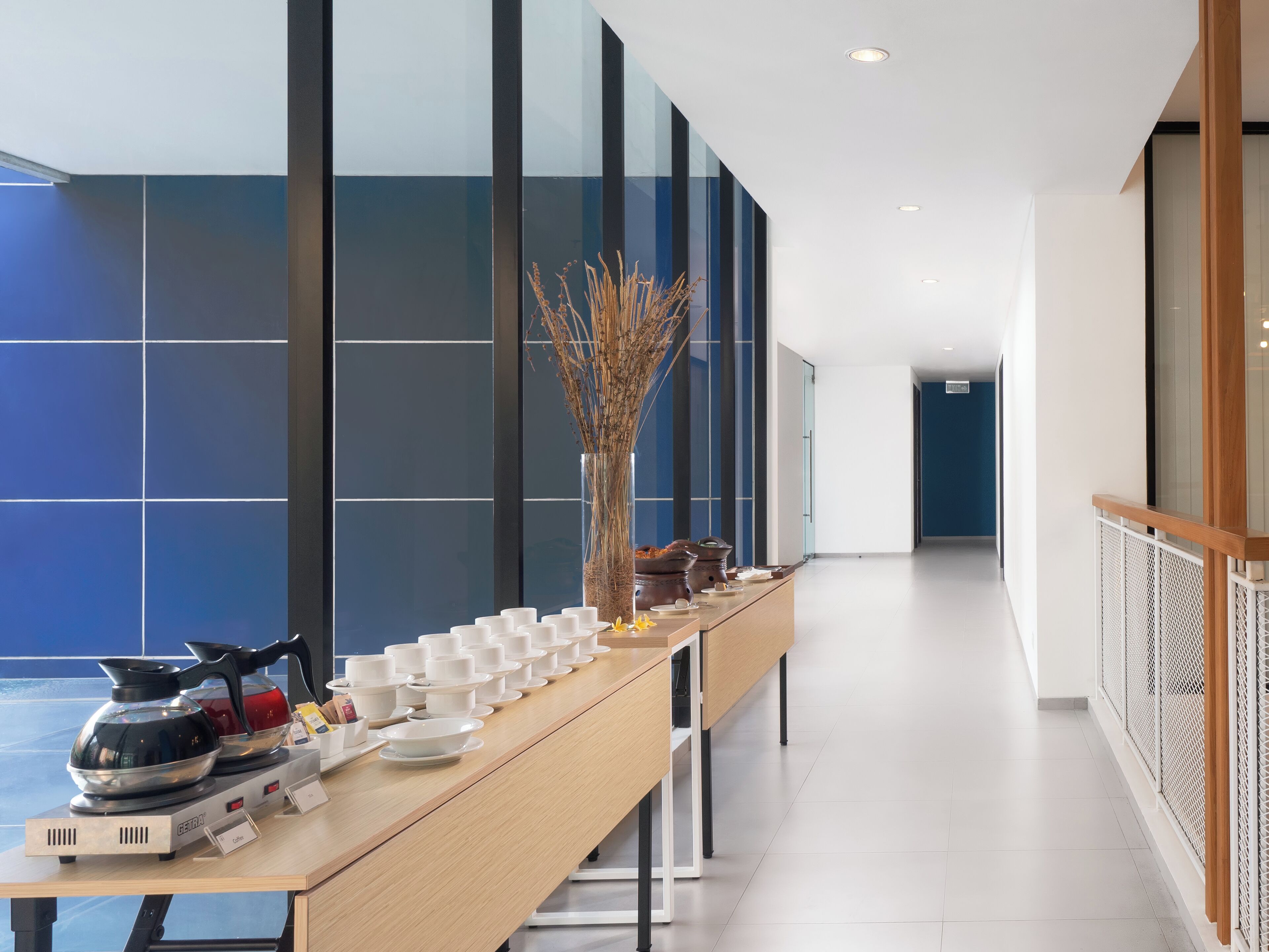 A modern hotel corridor with a long reception table displaying various tea and coffee equipment.