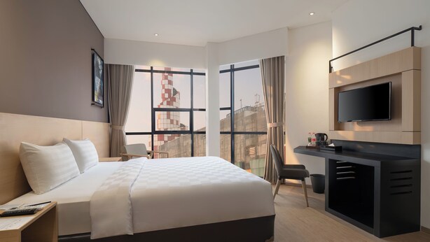 A modern hotel room with a large bed, a desk with a TV, and a city view. - Hotel 88 Blok M Jakarta by WH (Jakarta)